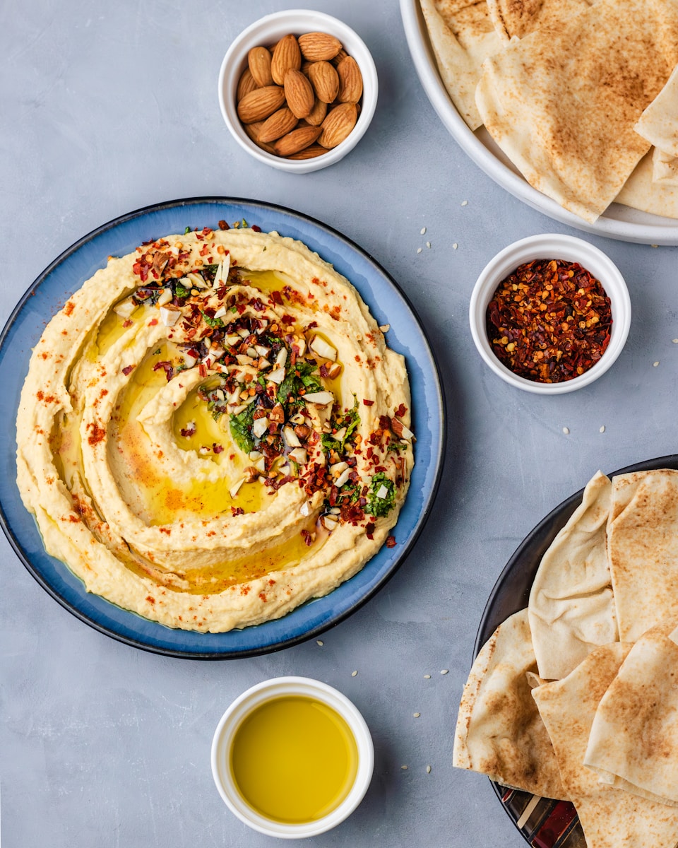 Hummus mit Pinienkernen - a plate of hummus, pita bread, and a bowl of olive oil